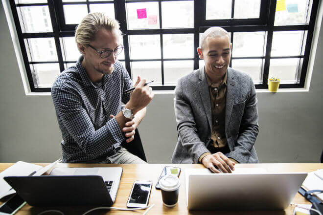 The photo is showing two persons sitting in front of two laptops in teaching
